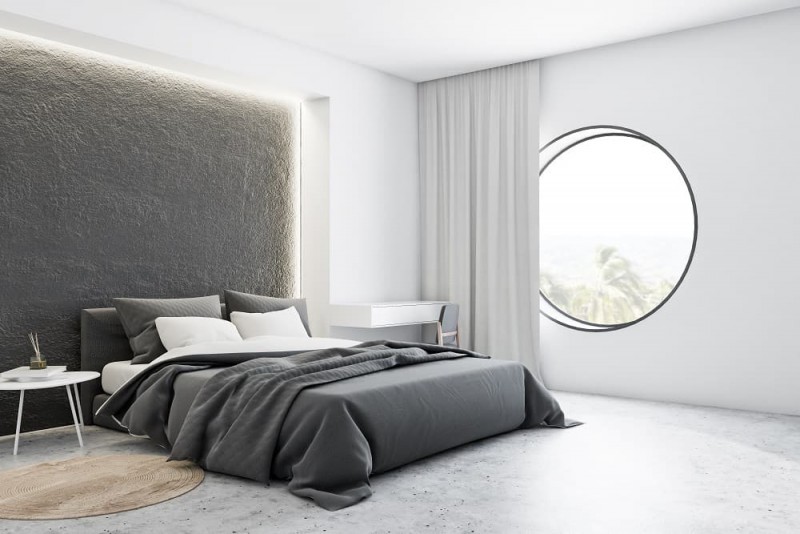 biała sypialnia z betonową ścianą za ł&oacute;żkiem i czarną pościelą